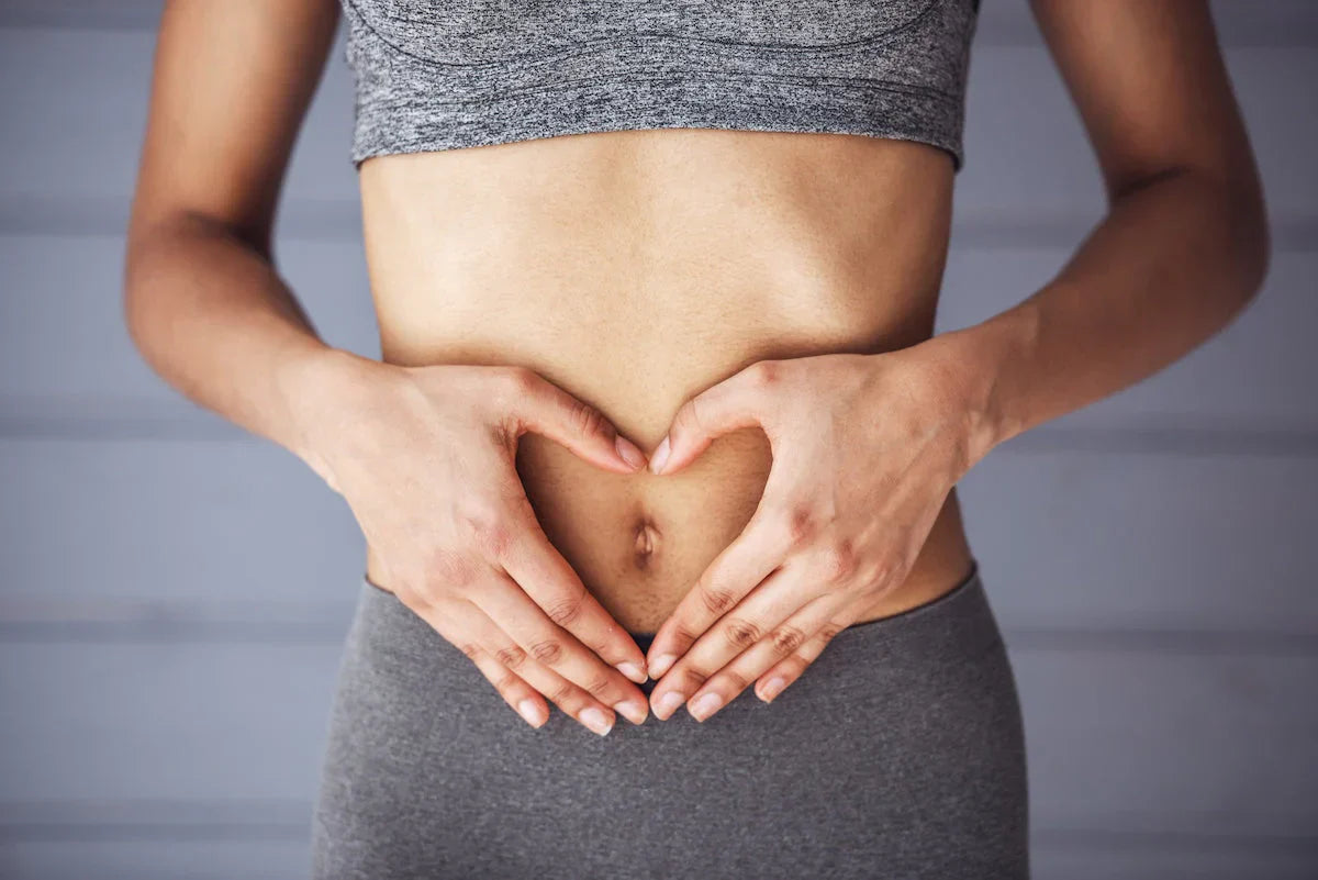 Fit woman in sportswear making a heart shape with her hands over her stomach, symbolizing health and wellness.