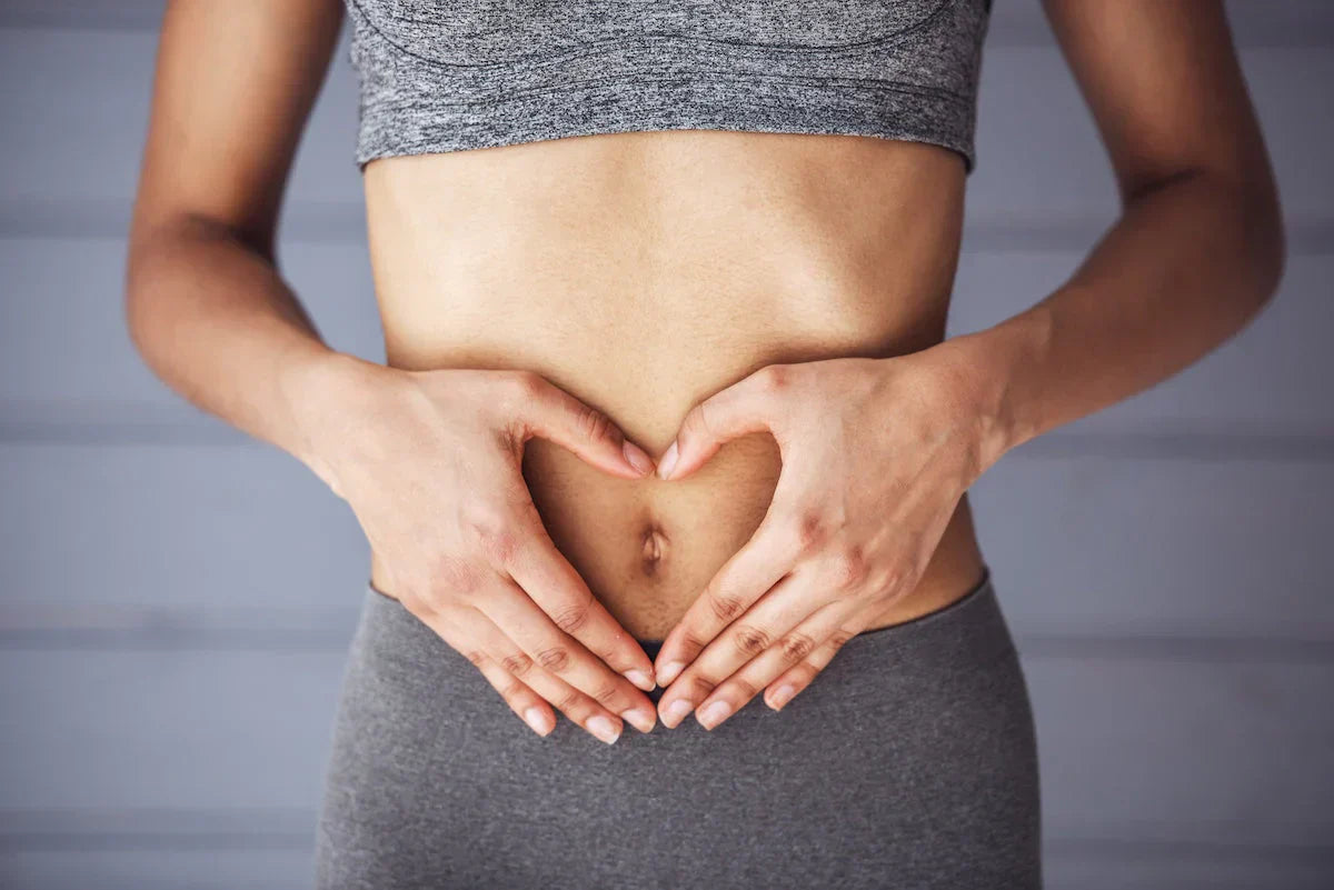 Fit woman in sportswear making a heart shape with her hands over her stomach, symbolizing health and wellness.