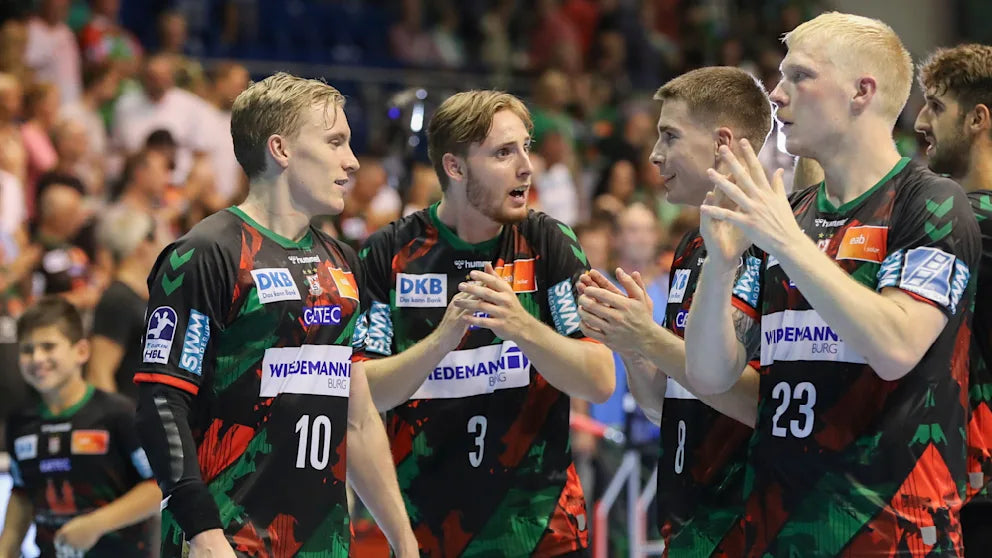 SC Magdeburg handball players in team uniforms celebrating on the court after a match, clapping and engaging with each other in front of a cheering crowd.