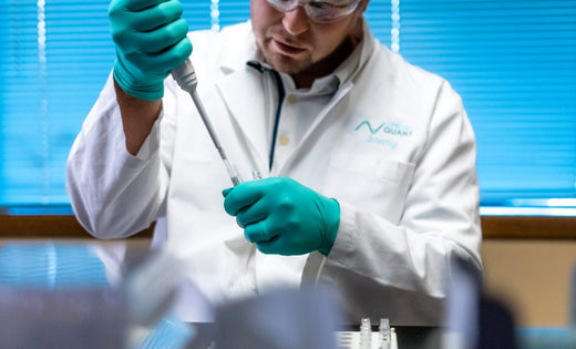 Scientist in a white lab coat and teal gloves using a pipette in a laboratory setting, conducting scientific research or testing.