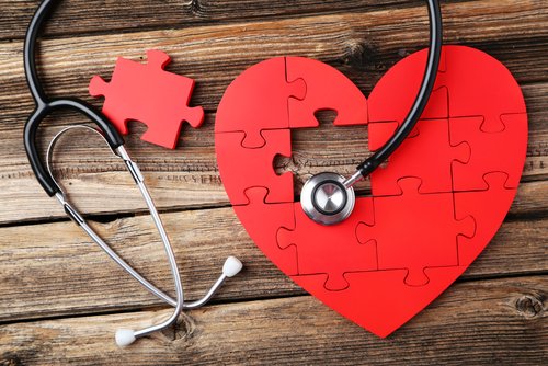 Red heart-shaped jigsaw puzzle with a missing piece, placed on a wooden surface next to a stethoscope.