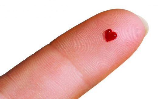 Close-up of a finger with a small, heart-shaped drop of blood on the fingertip.