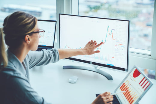 Woman analyzing stock market charts on multiple monitors in a modern office.