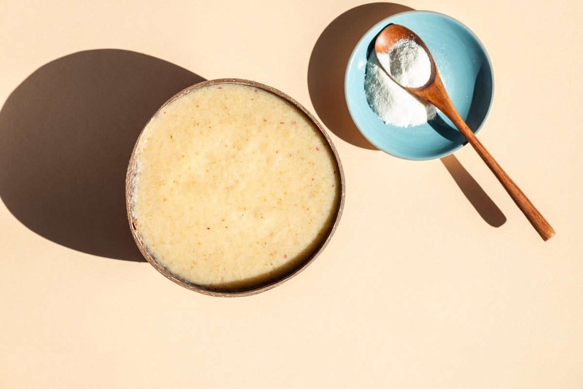 Collagen powder in a wooden spoon placed on a blue dish beside a smoothie bowl, representing collagen supplements as an alternative to bone broth.