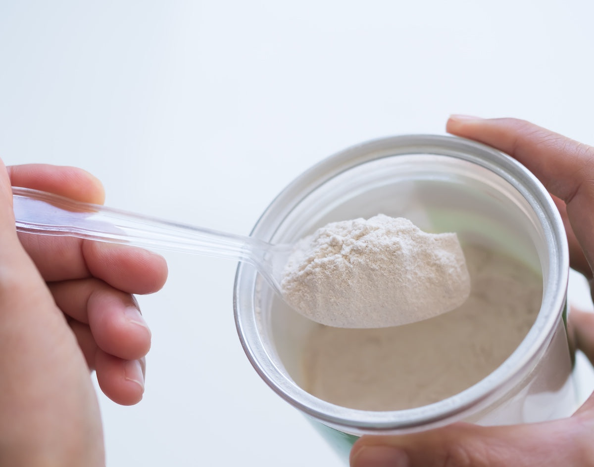 A person scooping a serving of white collagen powder from a container using a transparent plastic spoon.