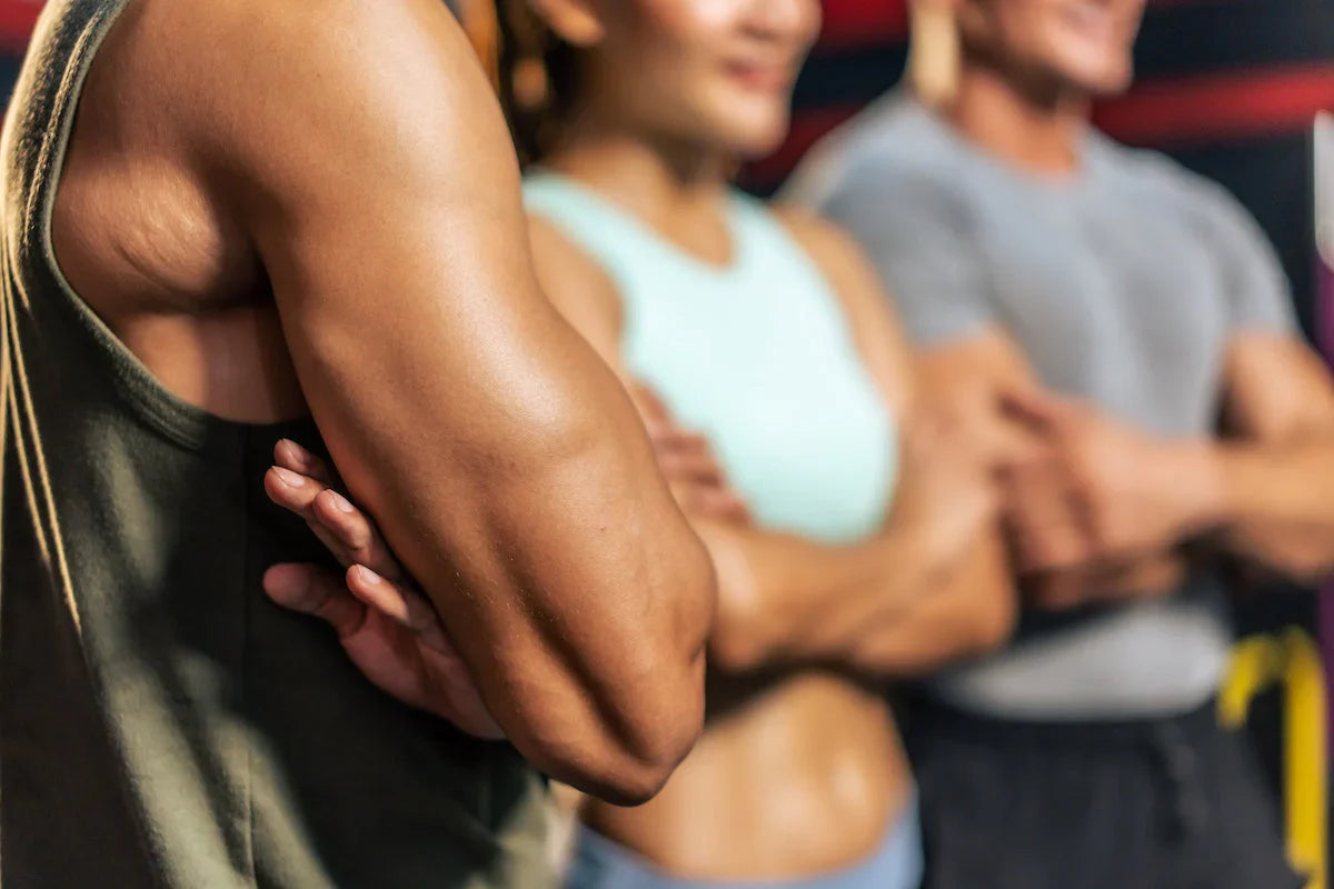 Group of fit young athletes in sportswear standing with crossed arms, showing muscular arms and toned bodies.