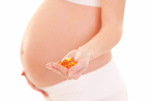 Pregnant woman in white holding a handful of omega-3 and prenatal supplement capsules, highlighting the importance of nutrition during pregnancy.
