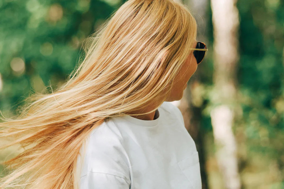 Close-up of a woman with long, healthy blonde hair flowing in the wind outdoors.