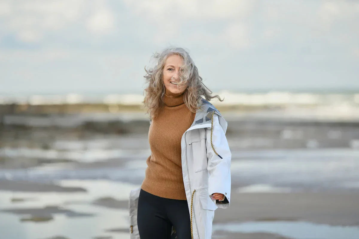 Woman standing on a beach wearing a brown sweater and white coat
