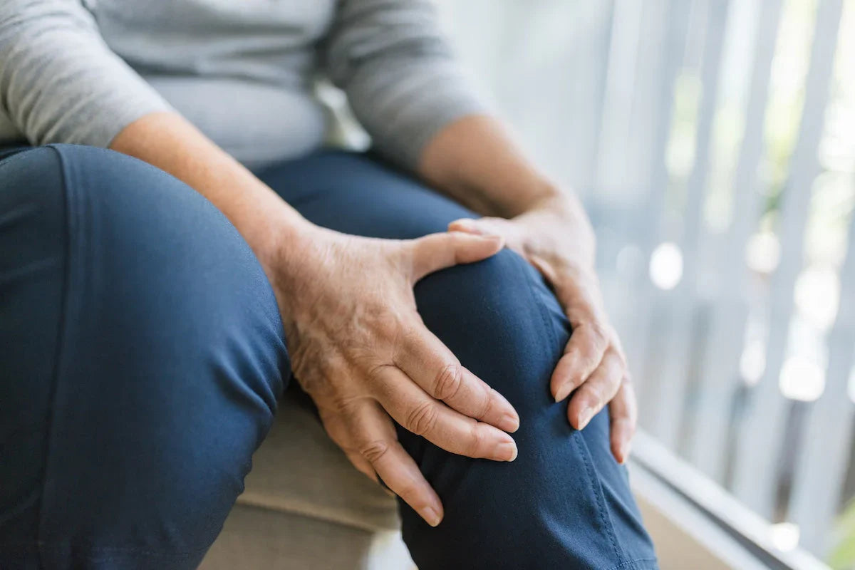Close-up of an elderly woman holding her knee with both hands, showing joint pain or arthritis discomfort.
