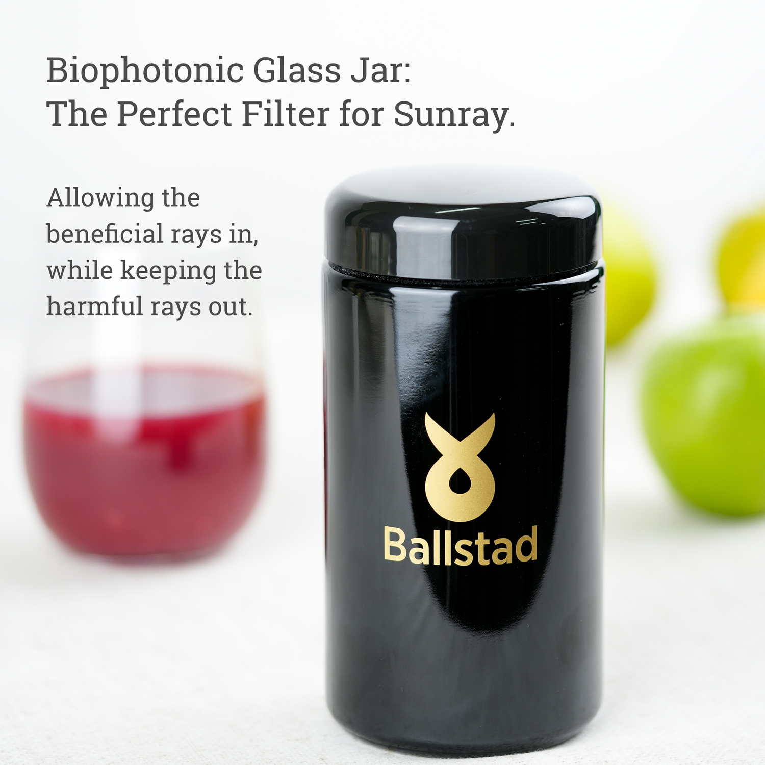 Black glass jar with gold logo and text about biophotonic properties, placed on a white background with blurred fruits.