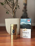 Gold canister and white box with blue label on a wooden surface, featuring Ballstad branding.
