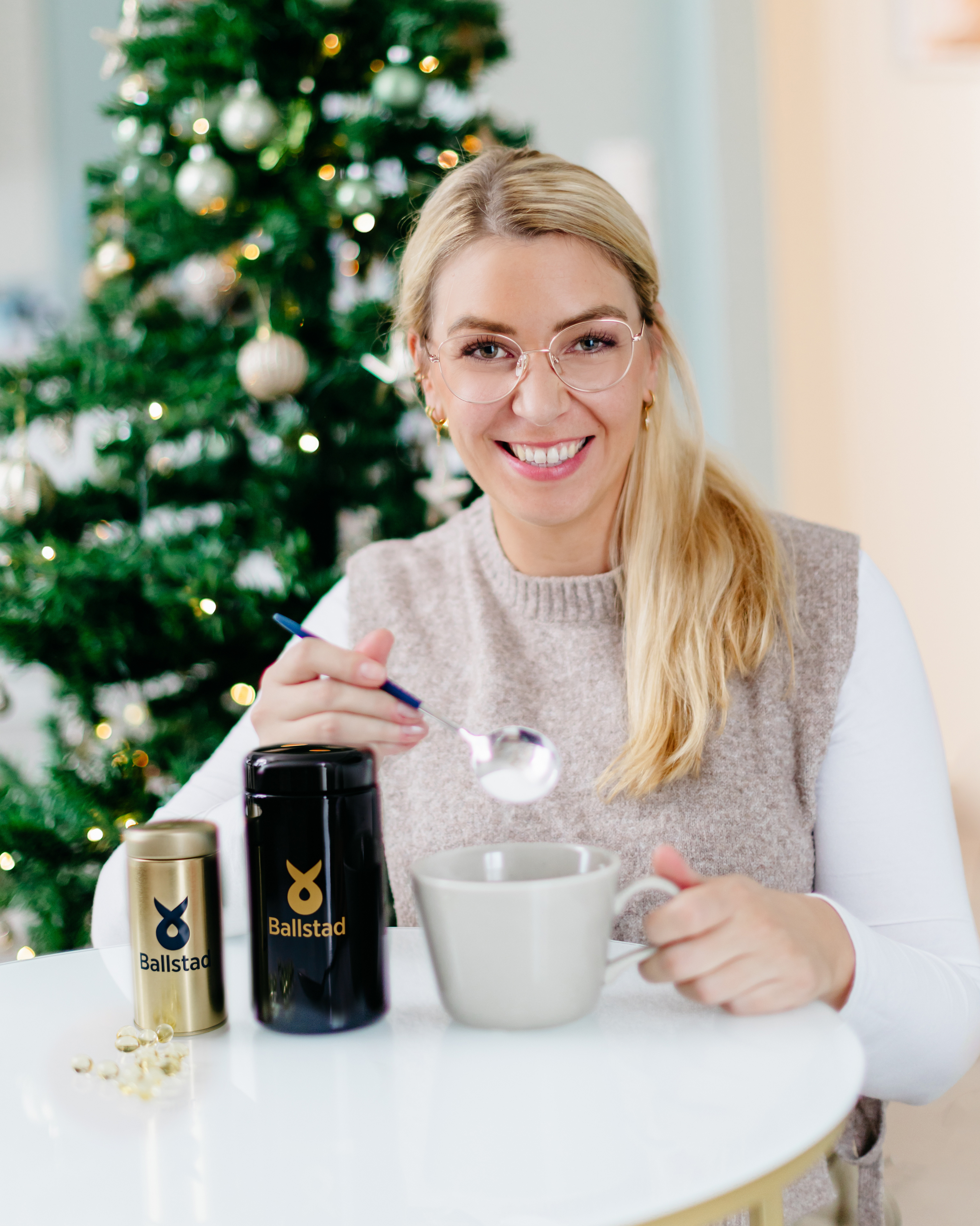 Woman sitting at a table with a coffee mug and a Ballistol can in front of a Christmas tree.